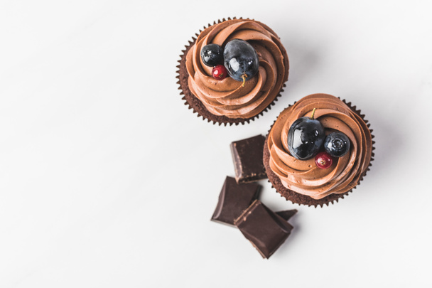 vista superior de cupcakes de chocolate con crema, uva, bayas y trozos de chocolate aislados en blanco
 - Foto, Imagen