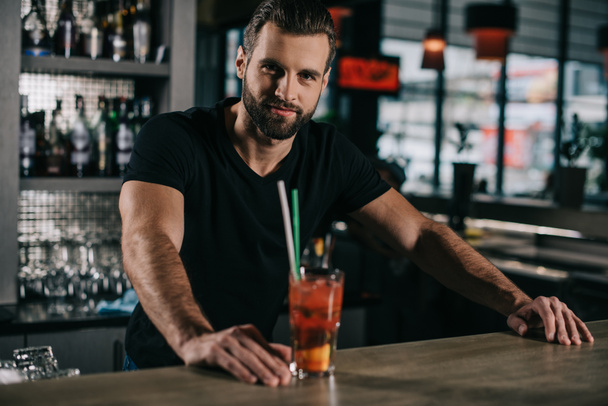 όμορφος μπάρμαν στέκεται με αλκοόλη ποτό στο μπαρ μετρητή - Φωτογραφία, εικόνα