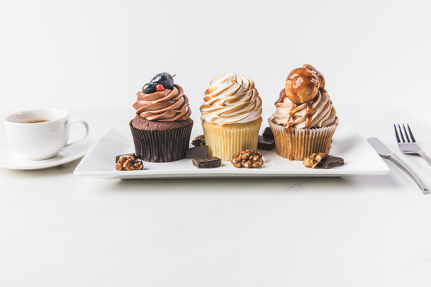 close up view of various cupcakes on plate, cup of coffee and cutlery isolated on white - Photo, Image