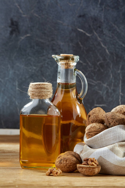 Aromatic oil in a glass jar and bottle with peanuts in bowl on wooden table, close-up, vertical - Photo, image