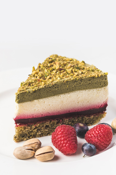 close up view of sweet cake with pistachios and berries on plate isolated on white - Φωτογραφία, εικόνα