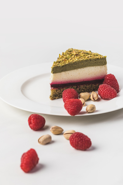 close up view of sweet cake with pistachios and raspberries on plate isolated on white - Zdjęcie, obraz