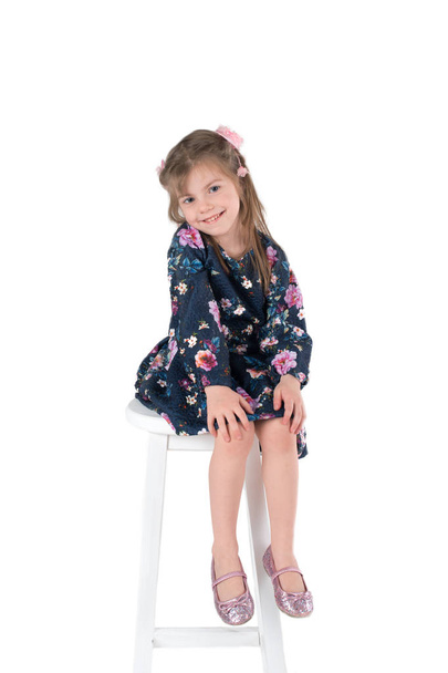elbiseli kız gülümser ve yüksek sandalye üzerinde oturur - Fotoğraf, Görsel