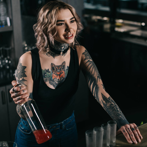 tattooed bartender holding bottle of alcohol and looking away - Φωτογραφία, εικόνα