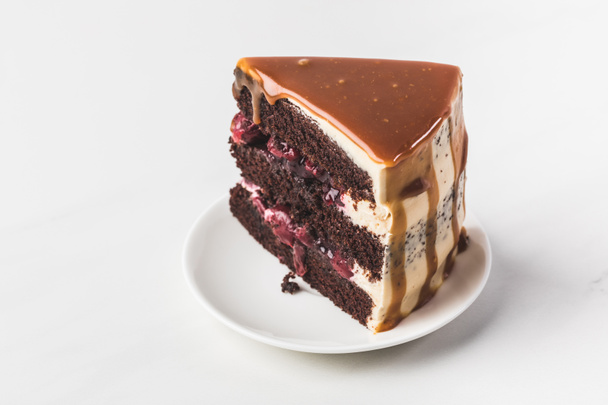Close-up van zoete kers-chocolade taart met karamel op plaat geïsoleerd op wit - Foto, afbeelding
