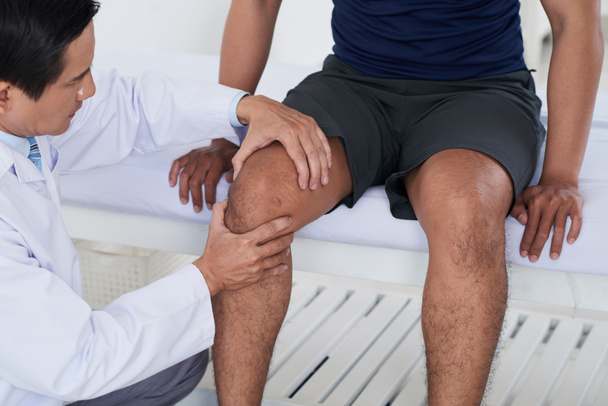 Doctor checking knee joint of male sportsman - Fotó, kép