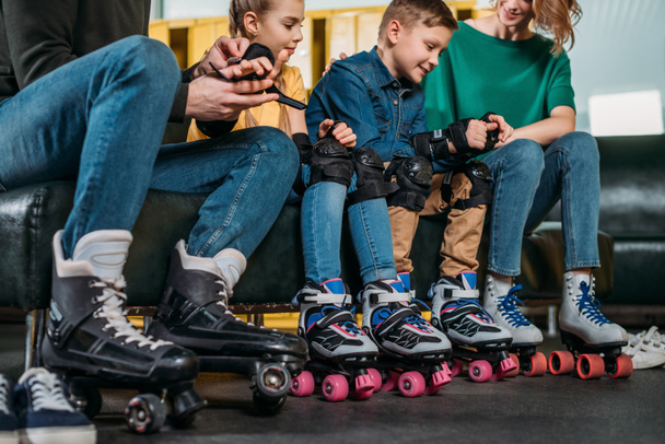 Μερική άποψη των γονέων που βοηθάει τα παιδιά να φορούν την προστασία πριν από το πατινάζ στο πάρκο skate - Φωτογραφία, εικόνα