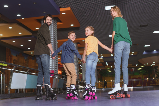 back view of family holding hands while skating on roller rink together - Foto, immagini