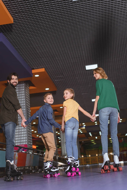 back view of family holding hands while skating on roller rink together - 写真・画像
