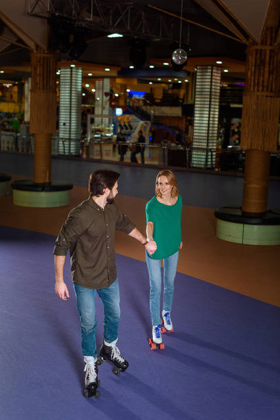young couple holding hands while skating together on roller rink - Photo, Image
