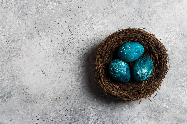 Πασχαλινά αυγά σε φωλιά ζωγραφισμένα στο χέρι με μπλε χρώμα επάνω ελαφρύς υπόβαθρο - Φωτογραφία, εικόνα