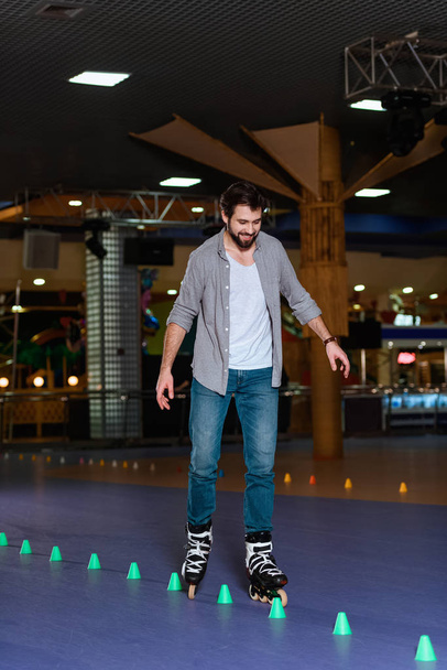 smiling man in roller skates skating on roller rink with cones - Фото, изображение