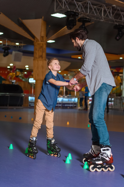 father and son skating together on roller rink with cones - Photo, Image