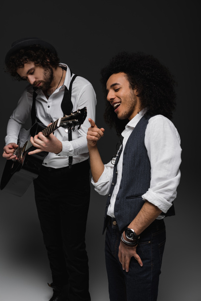 young duet of musicians playing guitar and singing on black - Foto, imagen