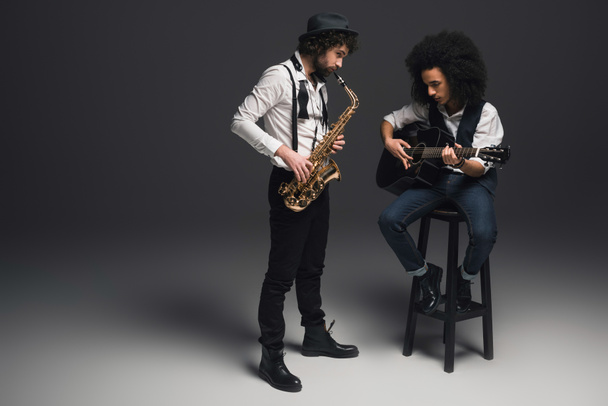 Stylový duet hudebníků hrajících saxofon a akustickou kytaru na černém pozadí - Fotografie, Obrázek