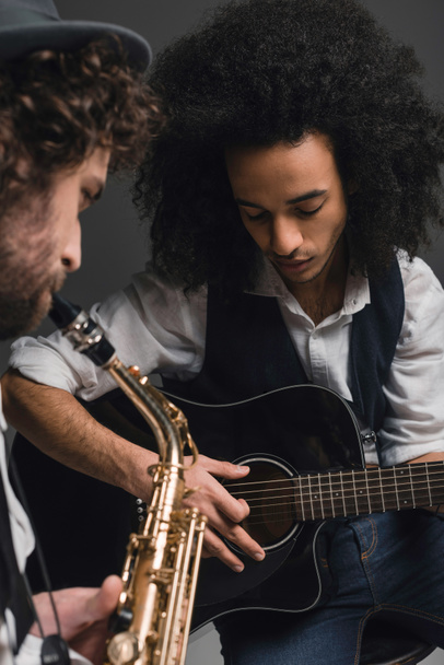 young duet of musicians playing sax and acoustic guitar on black - Fotó, kép