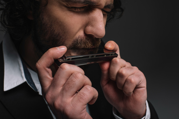 Close-up πορτρέτο της εκφραστική μουσικός που παίζει φυσαρμόνικα σε μαύρο - Φωτογραφία, εικόνα