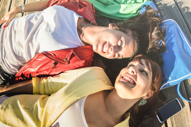 Вид зверху на щасливих усміхнених подружок, що лежать на підлозі в мить розслаблення концепція дружби з жіночими моделями відпочиває на фотосесії - Сучасний спосіб життя з кращими друзями - Яскравий теплий фільтр
 - Фото, зображення