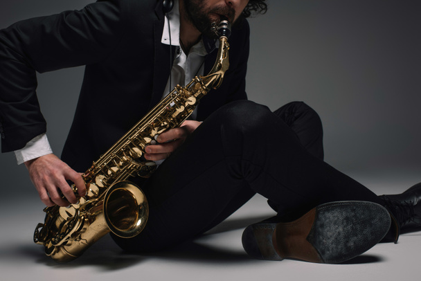 recortado disparo de músico tocando saxofón mientras está sentado en el suelo
 - Foto, imagen