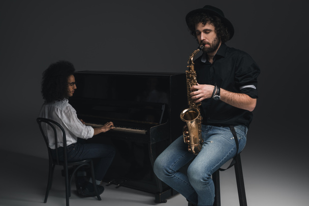 hombre tocando el saxofón mientras su compañero tocando el piano borroso en el fondo
 - Foto, imagen