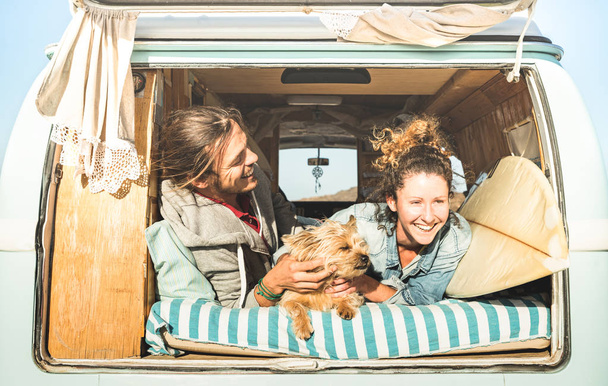 Hipster pareja con lindo perro viajando juntos en la vendimia mini van de transporte - Concepto de inspiración de vida con personas hippies en viaje de aventura en monovolumen en el momento de relax - Brillante cálido filtro retro
 - Foto, imagen