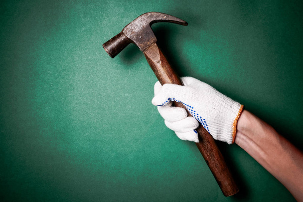 Hammer in hand with protection glove on green background. Free space for text - Φωτογραφία, εικόνα