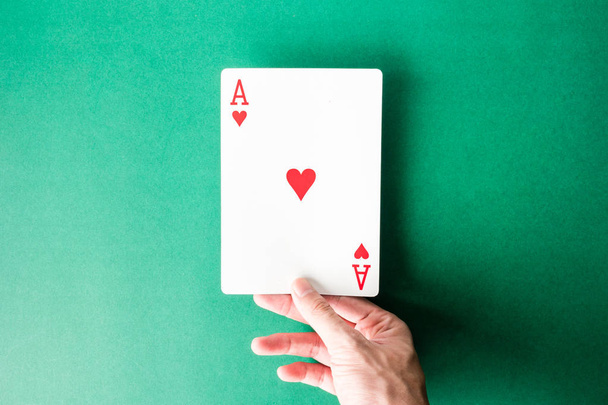 Hand holding a playing card on green background.  - 写真・画像