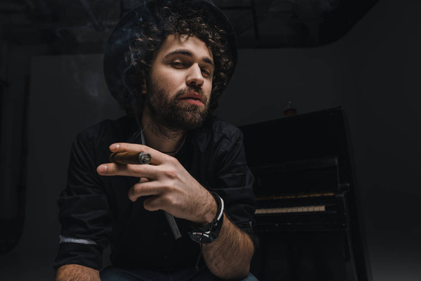 serious musician smoking cigar in front of piano on black - Photo, Image
