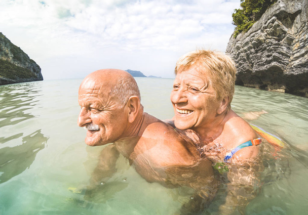 Senior couple vacationer having genuine playful fun on tropical beach in Thailand - Snorkel tour in exotic scenario - Active elderly and travel concept around the world - Warm afternoon bright filter - Photo, Image
