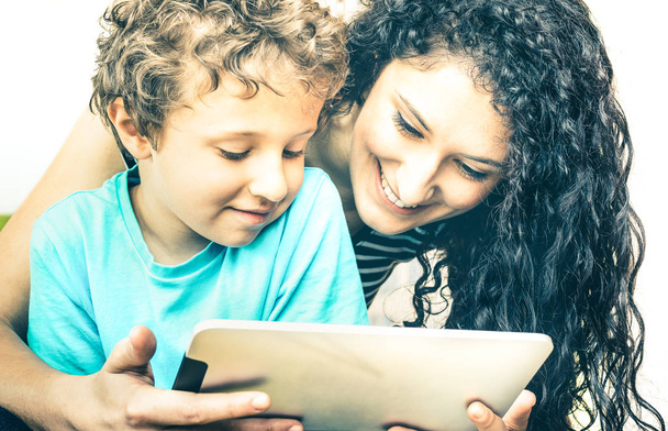 junge Mutter hat Spaß mit Sohn mit Tablet im Bett - Computertechnik lernen mit Schwester im Kinderzimmer - Lehrer zeigt Jungen, wie man mit modernem Gerät interagiert - weicher entsättigter Kontrastfilter - Foto, Bild