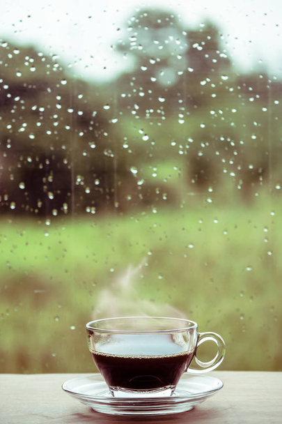 Kuppi kahvia pöydällä ikkunan sisällä, kahvitauko aamulla sadepäivä, rentouttava ja virkistävä käsitteitä
. - Valokuva, kuva