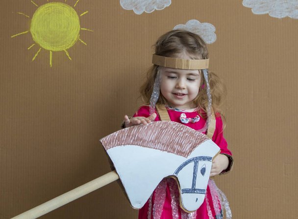 Young girl on stick horse. Handmade. Background of painted sun and white clouds - Photo, Image