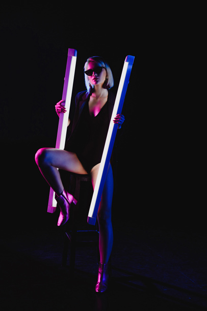 stylish beauty posing with two ultra violet lamps for fashion shoot, isolated on black - Foto, immagini