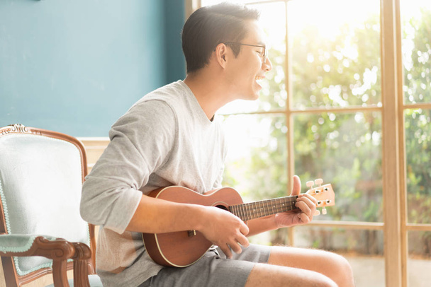 Asian young man hands playing acoustic guitar ukulele at home. E - Foto, Bild