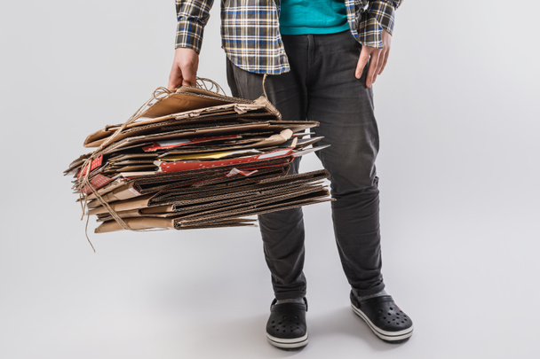 περικοπεί shot του ανθρώπου που κρατώντας σωρός του διπλωμένα κουτιά από χαρτόνι που απομονώνονται σε γκρι, ανακύκλωση έννοια - Φωτογραφία, εικόνα