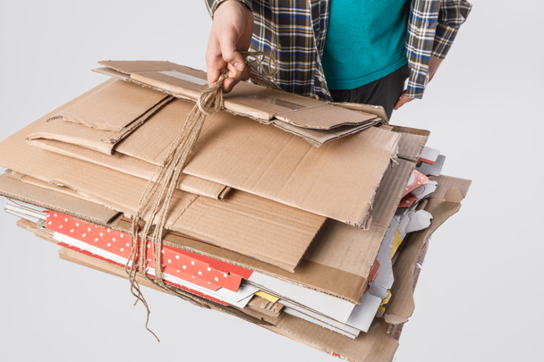 abgeschnittene Aufnahme eines Mannes mit einem Stapel gefalteter Kartons isoliert auf grauem Papier, Recyclingkonzept - Foto, Bild