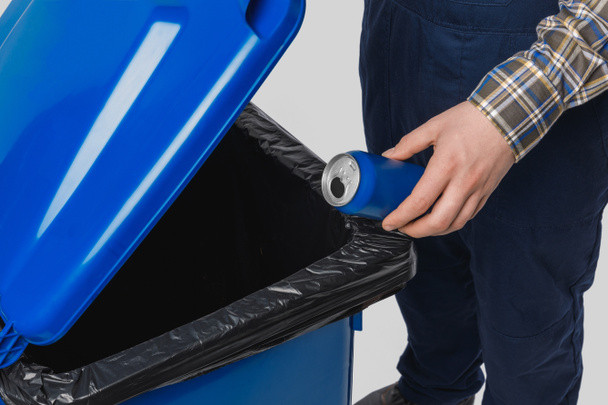 частичный вид уборщика, помещающего банку в мусорный бак, изолированный на сером
 - Фото, изображение