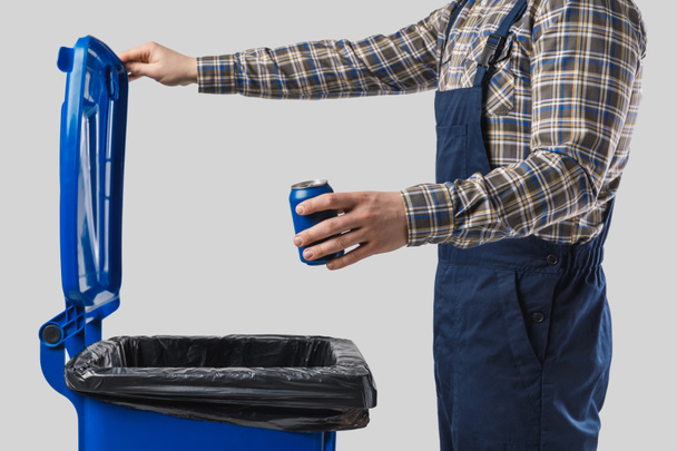 partial view of cleaner putting can into trash bin isolated on grey - Foto, Bild