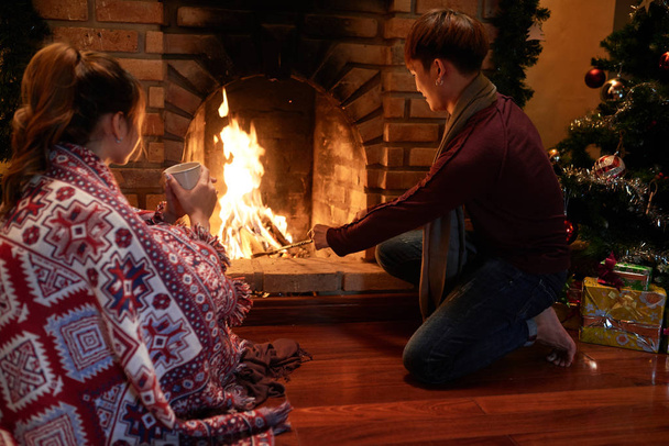 クリスマスの夜に燃えてそれを保つ人は暖炉に木を追加します。 - 写真・画像