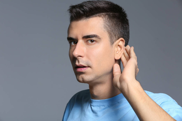Young man with hearing problem on grey background - Фото, зображення