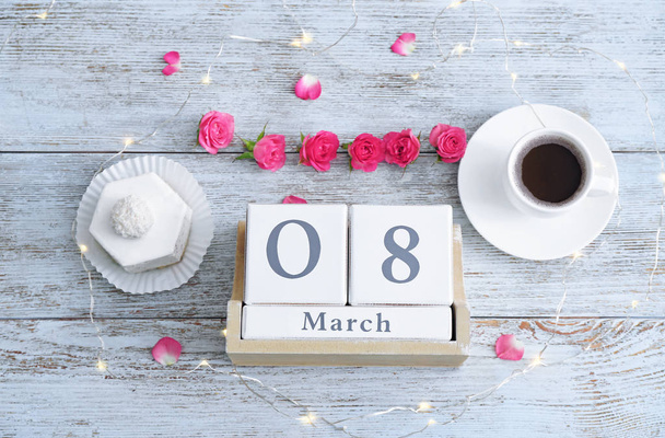 Wooden block calendar, flowers, dessert and cup of coffee on table. International Women's Day celebration - 写真・画像