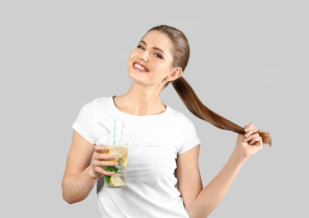 Beautiful young woman with glass of lemonade on grey background - Fotó, kép