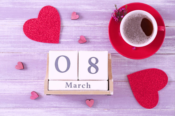 Wooden block calendar and cup of coffee on table. International Women's Day celebration - 写真・画像