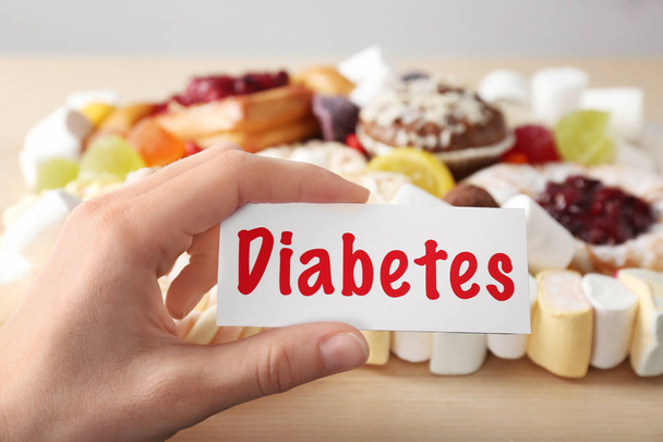 Woman holding card with word DIABETES over sweets, closeup - Фото, изображение