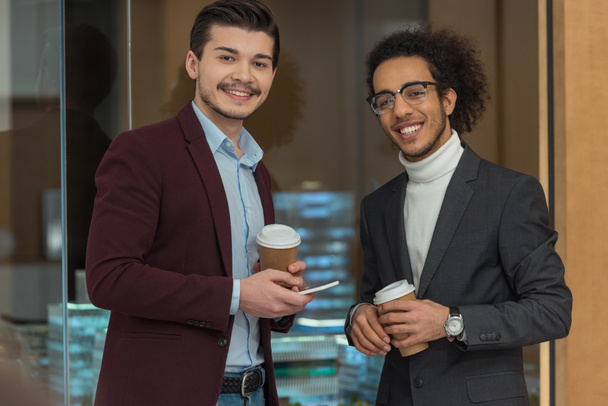 happy young businessmen with paper cups of coffee at office - Fotografie, Obrázek