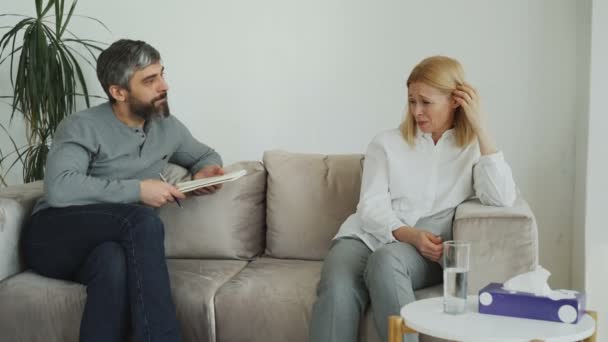 Male experienced psychologist talking and calm down depressed crying woman patient during psychotherapy session - Imágenes, Vídeo