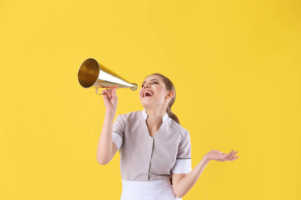Young chambermaid with megaphone on yellow background - Photo, image