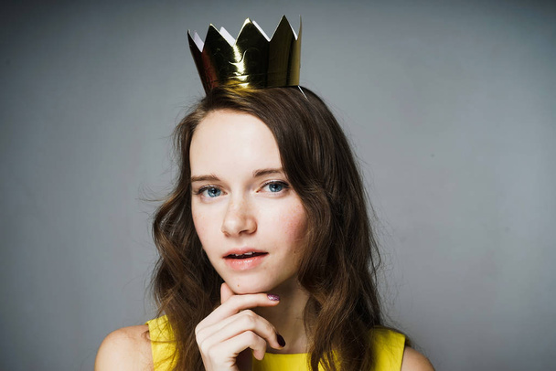 confident attractive girl in a yellow dress is waiting for Mother's Day, on her head is a golden crown - Fotografie, Obrázek