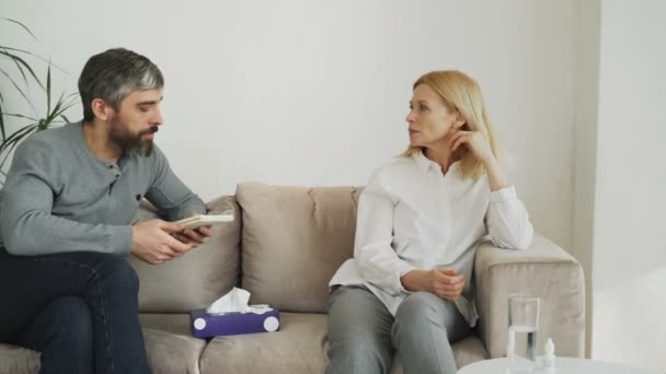 Crying stressed woman talking with professional male psychologist who gives paper tissue and trying to calm down her during thearpy session - Imágenes, Vídeo