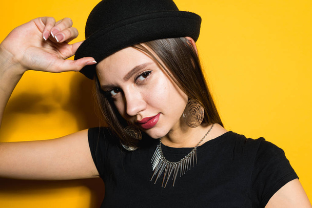 attractive beautiful girl in a black hat posing on a yellow background, on the neck expensive necklace - Foto, afbeelding